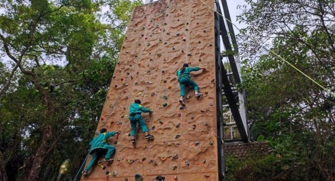 صورة لطلاب مدرسة إرشوي الإعدادية في تايوان وهم يتسلقون جدارًا صخريًا مرتفعًا ضمن منهاجهم الدراسي، يظهرون التركيز والإصرار.