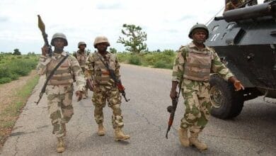 صورة جوية لقرية نيجيرية مدمرة بعد هجوم مسلح، مع وجود عناصر أمنية تقوم بالتحقيق في الأضرار والخسائر البشرية.