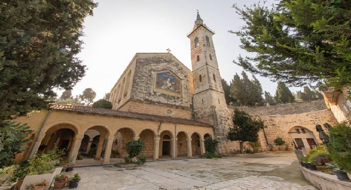 صورة خارجية لكنيسة الزيارة في قرية عين كارم بالقدس المحتلة، يظهر على جدرانها شعارات عنصرية مكتوبة بخط كبير، وعلامات تدنيس واضحة.