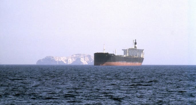 صورة جوية لسفينة تجارية تبحر في مياه زرقاء قبالة سواحل اليمن، مع إشارة رمزية لزورق صغير في المسافة، مما يوحي بالتوترات الأمنية في المنطقة.