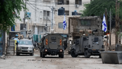 صورة تعبر عن وجود عسكري لاحتلال في بلدة فلسطينية، مع التركيز على قيود البناء والتوسع الاستيطاني.