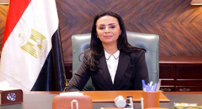 صورة لامرأة تقوم بسحب أموال من ماكينة صراف آلي، مع شعار وزارة التضامن الاجتماعي في الخلفية، ترمز لصرف الدعم النقدي الإضافي.