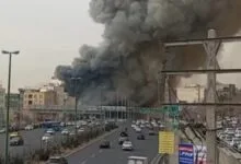 صورة جوية تظهر تصاعد أعمدة كثيفة من الدخان الأسود فوق منطقة باراند قرب العاصمة الإيرانية طهران، مع تجمعات سكنية ومناطق مفتوحة حول موقع الحريق.