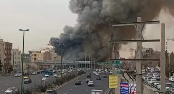 صورة جوية تظهر تصاعد أعمدة كثيفة من الدخان الأسود فوق منطقة باراند قرب العاصمة الإيرانية طهران، مع تجمعات سكنية ومناطق مفتوحة حول موقع الحريق.