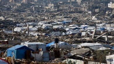 صورة جوية لمخيمات النازحين في قطاع غزة خلال شهر رمضان، تظهر خياماً متلاصقة بين ركام المباني المدمرة، مع أطفال يتجمعون حول نقطة توزيع مساعدات إنسانية من الأونروا.