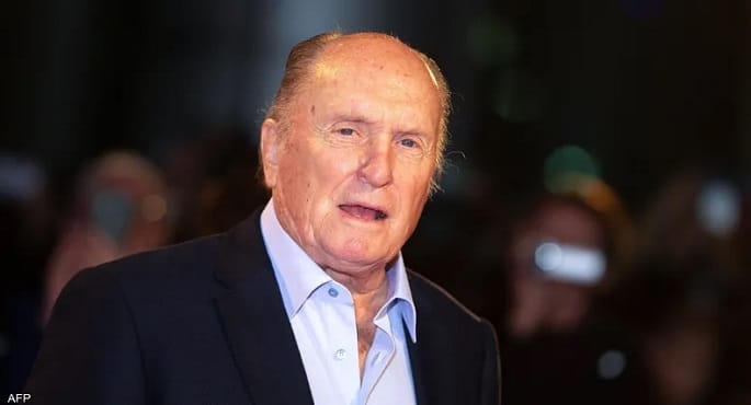 صورة للممثل الأمريكي الراحل روبرت دوفال، يظهر فيها بملامح جادة وتعابير وجه حكيمة، تعكس خبرته الطويلة في مجال التمثيل السينمائي.