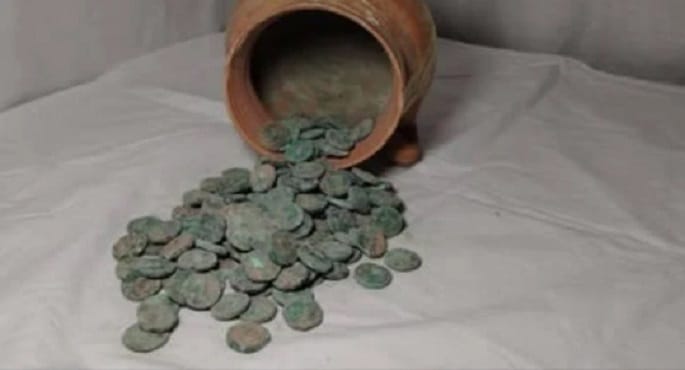 صورة مقربة لعملات معدنية نحاسية قديمة شديدة التأكسد من العصر الكوشاني، ربما في وعاء خزفي صغير، تمثل اكتشافاً أثرياً تاريخياً.