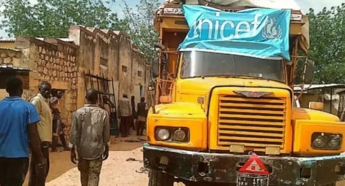 صورة لقافلة مساعدات إنسانية تابعة للأمم المتحدة تسير على طريق وعر في منطقة ريفية سودانية، مع أشخاص محليين يستقبلون الشحنات، ترمز لوصول الإغاثة بعد فترة طويلة من الانقطاع.