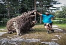 منحوتة ضخمة لحيوان أسطوري مصنوعة بالكامل من أغصان وأخشاب الأشجار المتساقطة، تقع في غابة خضراء، تُظهر تفاصيل دقيقة وتناغمًا مع البيئة المحيطة.